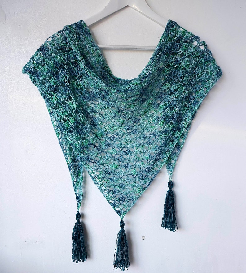 May include: A teal and green crocheted shawl with a triangular shape and fringe tassels.