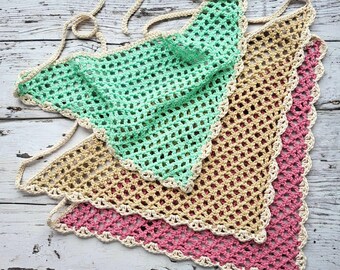 May include: Three handmade crochet triangle scarves in shades of mint green, tan, and pink. Each scarf features a scalloped edge and a cream-colored border. The scarves are displayed on a weathered, light-colored wooden surface.