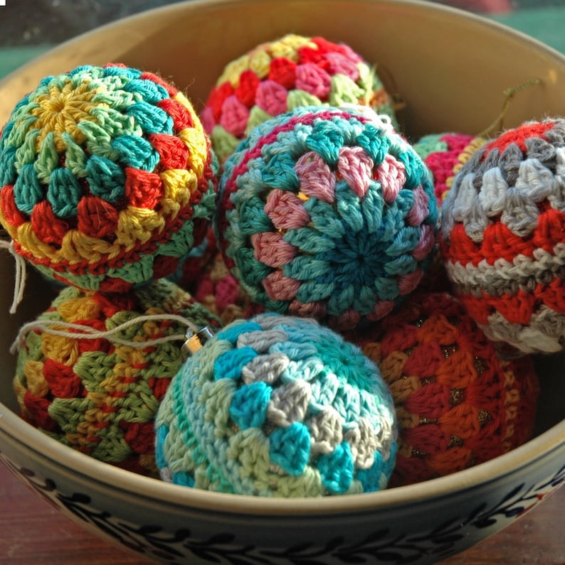 May include: A bowl filled with colorful crocheted ornaments. The ornaments are made in a variety of colors, including red, blue, green, yellow, and white. They are all crocheted in a square pattern.