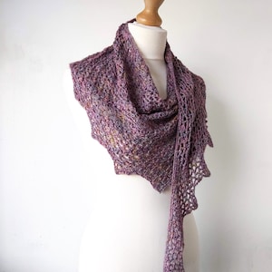 Puede incluir: Un chal de ganchillo morado y marr&oacute;n con un dise&ntilde;o de encaje. El chal est&aacute; drapeado sobre un maniqu&iacute; blanco.