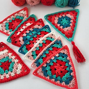 Pode incluir: Peças triangulares de crochê coloridas em tons de vermelho, turquesa e rosa. O trabalho de crochê apresenta um padrão floral e está disposto sobre uma superfície branca. Uma borla vermelha está presa a um dos triângulos. Meadas de lã são visíveis no fundo.