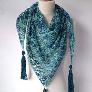 May include: A teal and green crocheted shawl with fringe tassels. The shawl is triangular in shape and has a delicate openwork design.