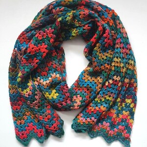 May include: A colorful, handmade crochet scarf. The scarf features a vibrant mix of red, blue, green, yellow, and orange yarn, creating a patchwork design. The edges have a scalloped trim. This cozy accessory is perfect for adding a pop of color to any outfit.
