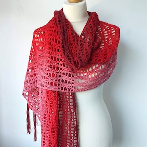 May include: A red and pink ombre crochet scarf with fringe on the ends. The scarf is draped over a white mannequin.