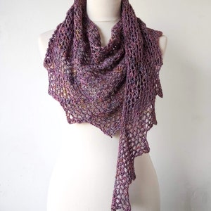 Puede incluir: Un chal de ganchillo morado y marr&oacute;n con un dise&ntilde;o de encaje. El chal est&aacute; drapeado sobre un maniqu&iacute; blanco.