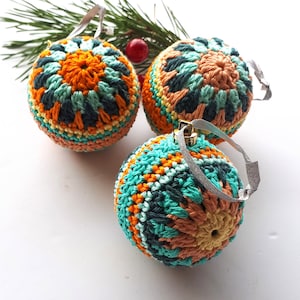 May include: Three crocheted Christmas ornaments in teal, orange, and yellow. The ornaments have a geometric pattern and are decorated with silver glitter.