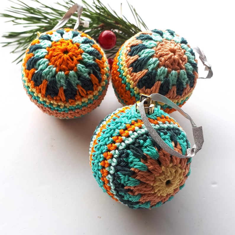 May include: Three crocheted Christmas ornaments in teal, orange, and yellow. The ornaments have a geometric pattern and are decorated with silver glitter.