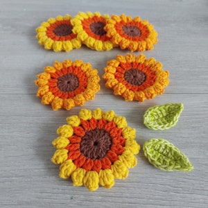 May include: Six crocheted sunflower coasters in shades of yellow, orange, and brown, with two green crocheted leaves.