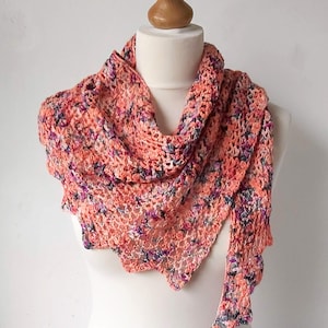 Puede incluir: Un chal de ganchillo de color melocot&oacute;n con un patr&oacute;n floral. El chal est&aacute; drapeado sobre un maniqu&iacute; blanco.