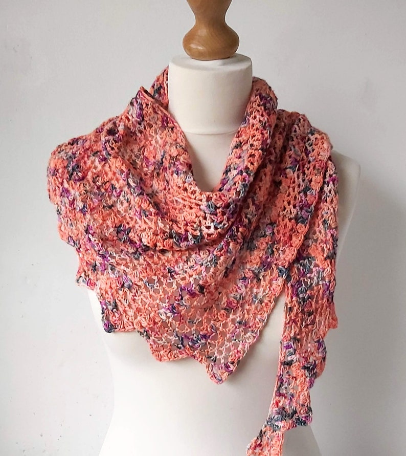 Puede incluir: Un chal de ganchillo de color melocot&oacute;n con un patr&oacute;n floral. El chal est&aacute; drapeado sobre un maniqu&iacute; blanco.