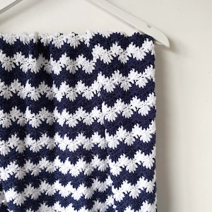 May include: A navy blue and white crocheted blanket with a chevron pattern. The blanket is hanging on a white hanger.