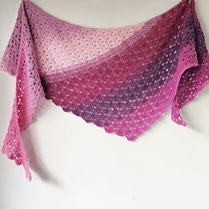 May include: A crocheted shawl in shades of pink, purple, and white. The shawl is made with a delicate stitch pattern and has a scalloped edge.