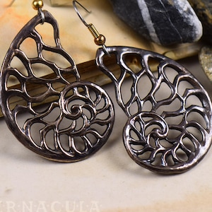 Può includere: Un paio di orecchini in bronzo a forma di conchiglie di nautilus con intricati disegni ritagliati.
