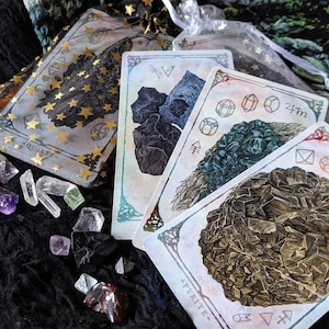 May include: Four tarot cards featuring different types of crystals. The cards are white with gold accents and feature illustrations of quartz, pyrite, and two other crystals. The cards are laid out on a black surface with various crystals scattered around them.