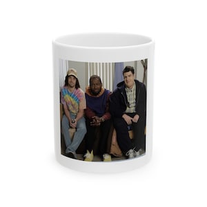 Può includere: Tazza in ceramica bianca con un'immagine di tre persone. L'immagine sulla tazza mostra tre uomini in abiti casual. La tazza è di dimensioni e forma standard, adatta per bevande calde.