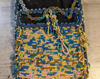 May include: A small beaded purse with a blue, yellow, and pink geometric pattern. The purse has a fringe border and a black fabric lining.