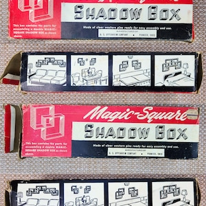 May include: A rectangular cardboard box for a Magic-Square Shadow Box. The red, white, and black packaging features line drawings of square shelving units and text detailing assembly parts, manufacturer information, and various room display ideas.