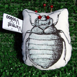 May include: A white pincushion shaped like a bug with red eyes and black and white details. The pincushion has the text "Bubble Opium Etsy.com" printed on the bottom and "Vermith Voodoo" printed on a tag.