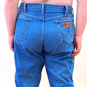 May include: A pair of blue denim jeans with a brown leather patch on the back pocket. The jeans have a high waist and a straight leg.