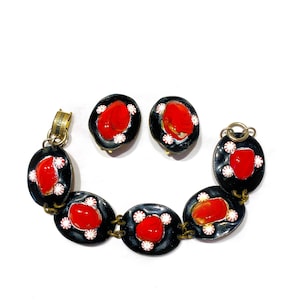 May include: A black enamel bracelet with red and white enamel accents. The bracelet has a clasp and is made up of five oval-shaped links. The set also includes a pair of matching earrings.