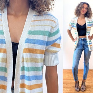 May include: A striped cardigan with short sleeves in white, blue, green, and orange. The cardigan has a V-neck and is open in the front.