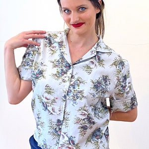 May include: A light blue short-sleeved button-up shirt with a floral print. The flowers are in shades of blue, green, and red.