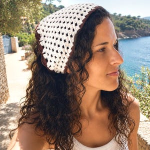 May include: A triangular crochet headscarf featuring a white openwork diamond pattern with a solid dark brown border. The headscarf is constructed with a textured yarn and is tied at the back of the head, covering the crown with a classic triangular shape.