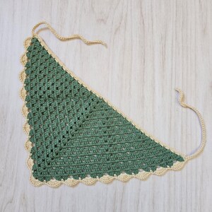 May include: A triangular crochet bandana featuring a sage green center with a textured openwork pattern and a scalloped cream-colored border. The accessory includes two thin crocheted ties at the top corners for securing the garment in place.