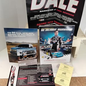 May include: A selection of racing promotional items. Features a large black poster with "DALE" in white, a magazine with a Chevy Silverado, and a DVD case with "10 Years Running" on it.