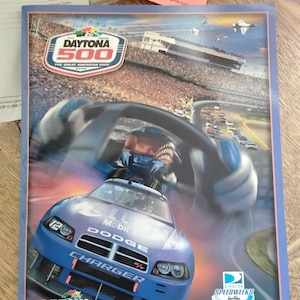Op de afbeelding: Souvenirprogramma van de Daytona 500 van 2009. De cover toont een blauwe Dodge Charger raceauto met het Mobil-logo, een coureur en het Daytona International Speedway-logo. Het programma is voor de race van 7 tot 15 februari 2009.