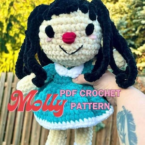Puede incluir: Muñeca de crochet con cabello negro, vestido turquesa y zapatos blancos. La muñeca sostiene un cartel que dice "PDF CROCHET PATTERN".