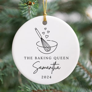 May include: White ceramic Christmas ornament with a black outline of a mixing bowl and whisk. The text "The Baking Queen Samantha 2024" is printed on the ornament.