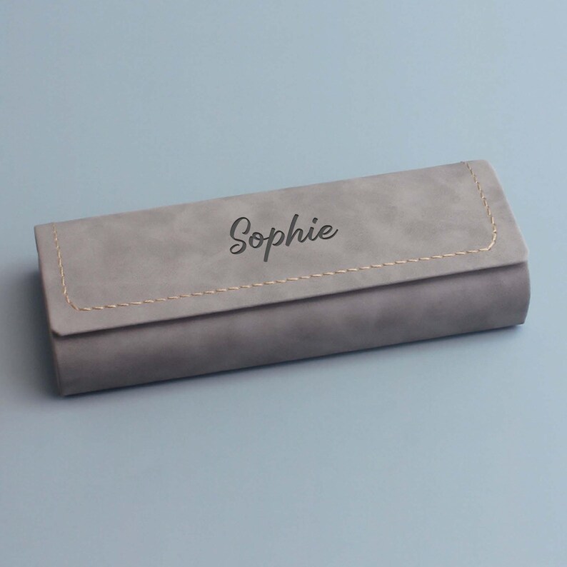 Peut inclure: Un &eacute;tui &agrave; lunettes rectangulaire, gris, doux, avec une couture cousue et le nom "Sophie" grav&eacute; sur le dessus.