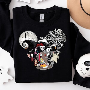 Puede incluir: Sudadera negra con dise&ntilde;o en forma de coraz&oacute;n con personajes de "Pesadilla antes de Navidad" y una luna llena. Incluye una telara&ntilde;a blanca, fantasmas y una taza con forma de calavera. Tambi&eacute;n se ve un sombrero color canela y la palabra "Boo".