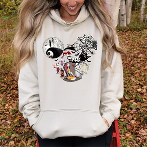 Puede incluir: Sudadera con capucha de color crema con un gr&aacute;fico de personajes de Pesadilla antes de Navidad. El dise&ntilde;o incluye a Jack Skellington, Sally y otros personajes, con una telara&ntilde;a y un fondo de luna. La sudadera tiene un bolsillo delantero y una capucha con cord&oacute;n.