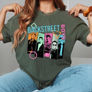 May include: Olive green t-shirt featuring the text "BACKSTREET BOYS" in a retro design. The graphic includes images of the band members in colorful rectangles. The shirt is a relaxed fit.