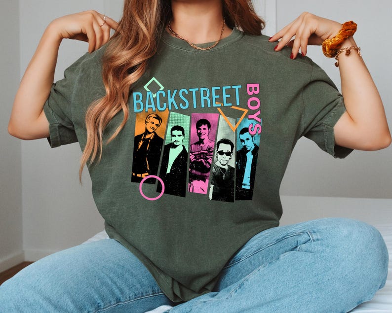 May include: Olive green t-shirt featuring the text "BACKSTREET BOYS" in a retro design. The graphic includes images of the band members in colorful rectangles. The shirt is a relaxed fit.