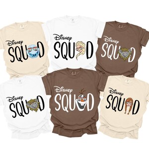 K&ouml;nnte beinhalten: Sechs kurz&auml;rmelige T-Shirts in verschiedenen Farben, darunter Wei&szlig;, Beige und Braun. Jedes Shirt tr&auml;gt den Text "Disney Squad" mit einer anderen Charaktergrafik. Zu den Charakteren geh&ouml;ren Elsa, Olaf, Anna und andere.