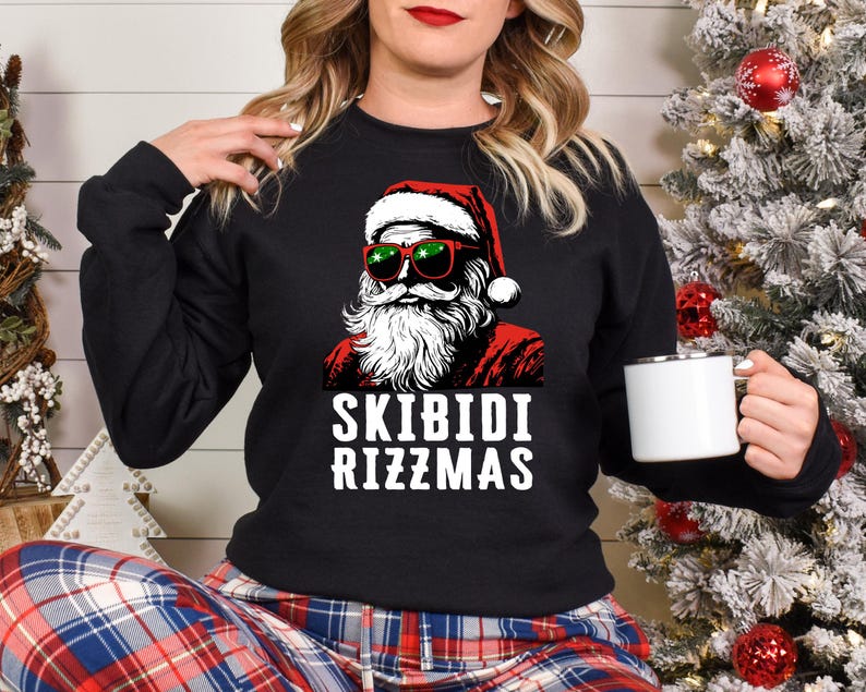 Puede incluir: Sudadera negra con un gr&aacute;fico de Santa Claus con gafas de sol y un gorro rojo. El texto "Skibidi Rizzmas" est&aacute; impreso debajo del gr&aacute;fico.