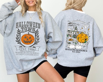 May include: Light gray sweatshirt with a Halloween Town graphic. The front features a pumpkin and text, "Halloween Town Est. 1998." The back has a similar design with a haunted house and pumpkin. A festive, seasonal apparel item.