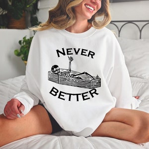 May include: White sweatshirt with a black graphic of a skeleton in a coffin with the text "NEVER BETTER" printed on it.