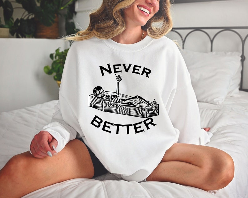 May include: White sweatshirt with a black graphic of a skeleton in a coffin with the text "NEVER BETTER" printed on it.
