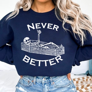 May include: A navy blue sweatshirt with a white graphic of a skeleton in a coffin with the text "NEVER BETTER".