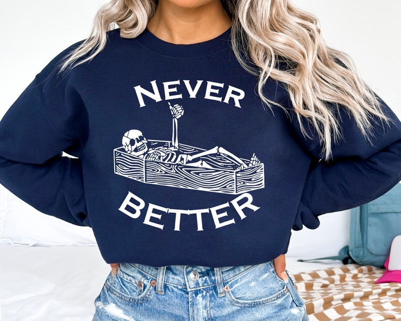May include: A navy blue sweatshirt with a white graphic of a skeleton in a coffin with the text "NEVER BETTER".