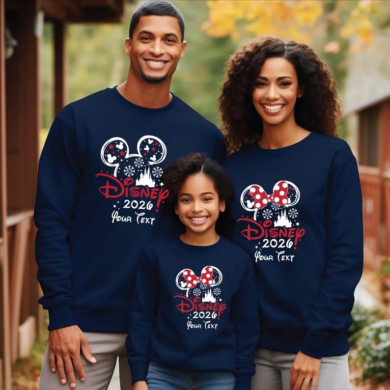 Puede incluir: Sudaderas azul marino con un dise&ntilde;o de Disney. El dise&ntilde;o incluye orejas de Mickey Mouse, copos de nieve, un castillo y el texto "Disney! 2026 Your Text" en rojo y blanco. Las sudaderas son usadas por una familia.