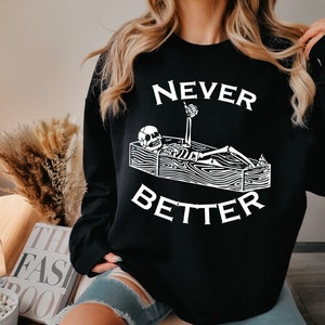 May include: Black sweatshirt with a white graphic of a skeleton lying in a coffin with the text "NEVER BETTER".
