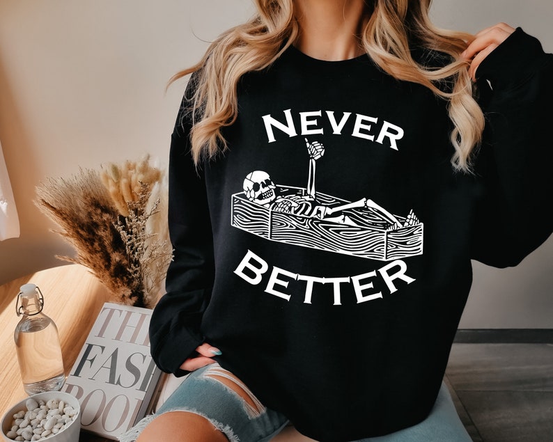 May include: Black sweatshirt with a white graphic of a skeleton lying in a coffin with the text "NEVER BETTER".