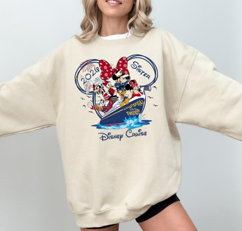 Puede incluir: Sudadera beige con un gr&aacute;fico colorido de personajes de Disney en un crucero. El dise&ntilde;o incluye a Minnie Mouse, el Pato Donald y Goofy, con las palabras "Disney Cruise" y "Sister" visibles.