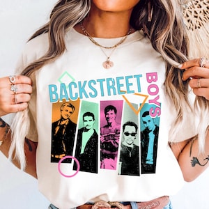 May include: Cream-colored t-shirt featuring the text "BACKSTREET BOYS" in a retro font with colorful geometric shapes. Below the text are five portrait illustrations of the band members in various poses and outfits. The shirt is a casual wear item.