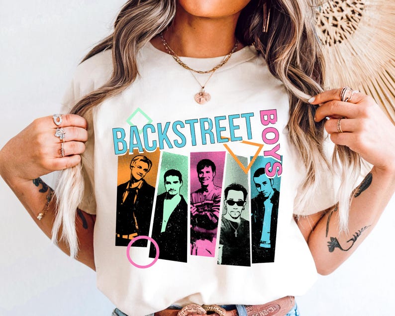 May include: Cream-colored t-shirt featuring the text "BACKSTREET BOYS" in a retro font with colorful geometric shapes. Below the text are five portrait illustrations of the band members in various poses and outfits. The shirt is a casual wear item.